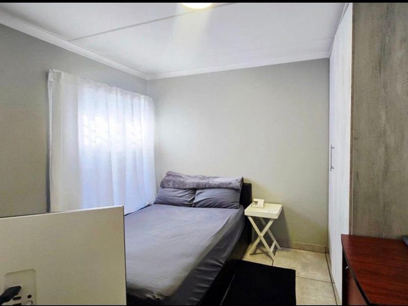 A compact bedroom featuring neutral wall tones, tiled flooring, and a built-in wardrobe, offering a functional and clean living space.