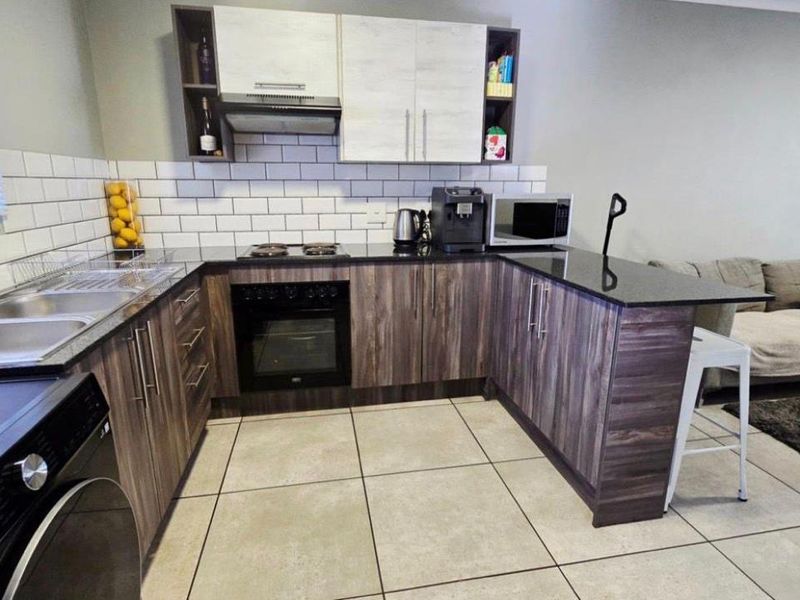 Modern open-plan kitchen featuring dark wood-grain cabinetry, granite countertops, subway tile backsplash, and integrated appliances, seamlessly flowing into the living area.