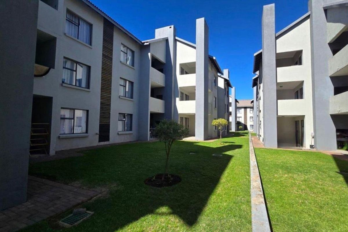 A well-maintained communal garden area situated between modern apartment blocks with paved walkways and manicured lawns.