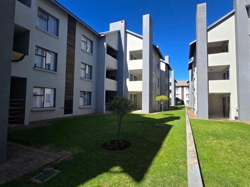A well-maintained communal garden area situated between modern apartment blocks with paved walkways and manicured lawns.