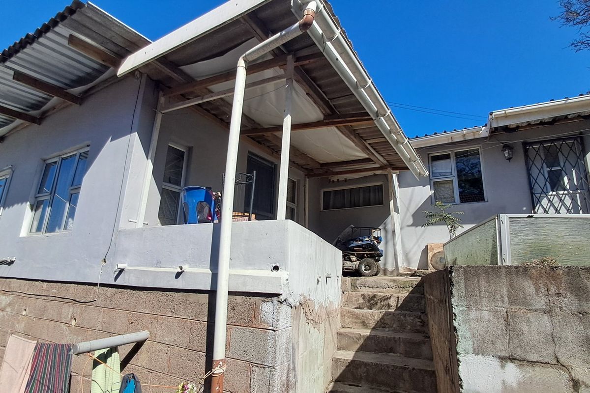Rear exterior view of the house featuring a covered patio area, concrete stairs, and a retaining wall with visible signs of weathering.