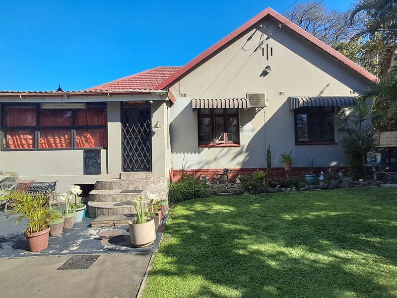 Front elevation of a single-story house featuring a tiled roof, security gate, and window awnings, set on a property with a lawn and driveway.