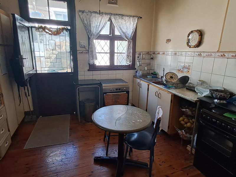 A dated kitchen featuring timber flooring, tiled splashbacks, and built-in cabinetry, offering significant potential for a modern renovation.