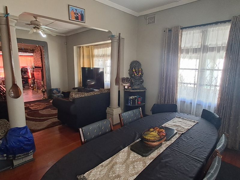 Open plan dining and living area featuring hardwood flooring, decorative columns, and an archway connecting to an adjacent room.