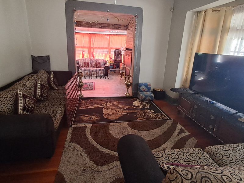 A living room featuring hardwood flooring and an arched entryway leading to an adjacent space, with natural light entering through a window with security bars.