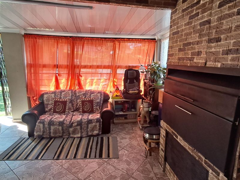 Covered patio area featuring a built-in braai, tiled flooring, and a brick feature wall, providing direct access to the garden.