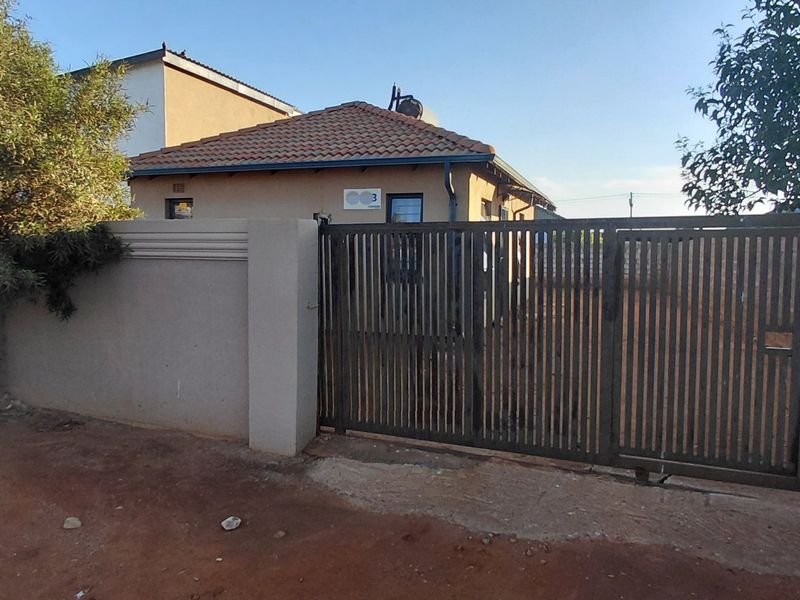 Front view of the property featuring a tiled roof, perimeter wall, and a metal sliding gate entrance.