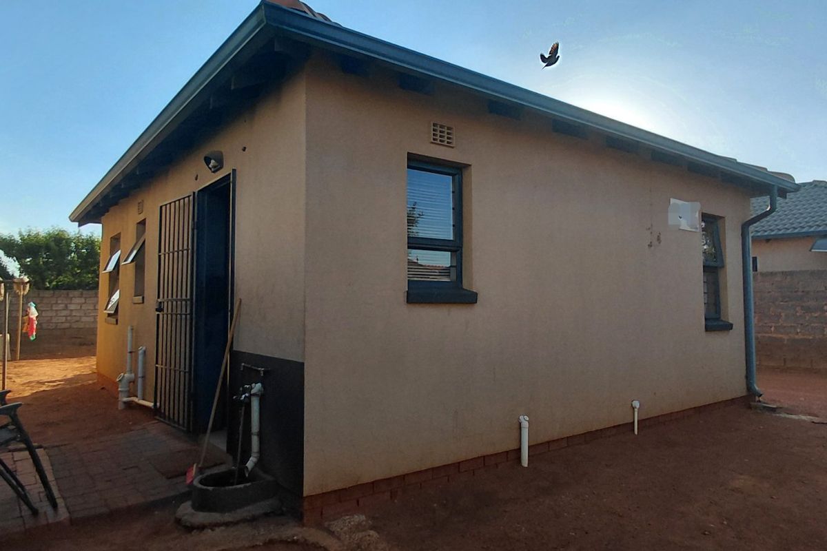 Rear view of the property showing the exterior wall, security gate, and surrounding yard area with boundary wall and electric fencing.