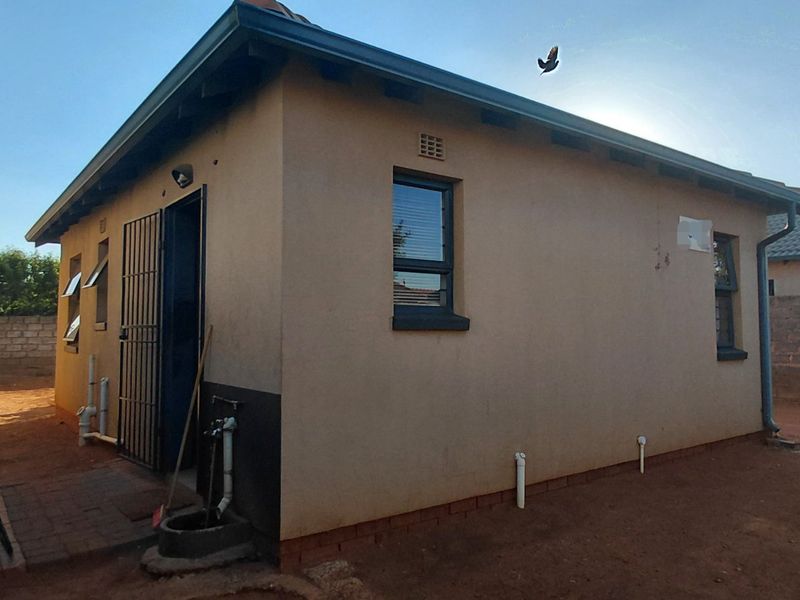 Rear view of the property showing the exterior wall, security gate, and surrounding yard area with boundary wall and electric fencing.