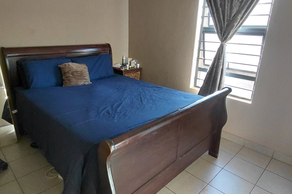 A functional bedroom featuring tiled flooring and a window fitted with security bars, providing natural light and basic utility.