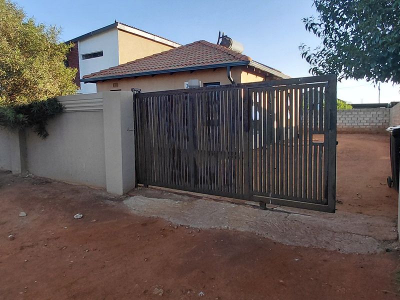 Front view of the property featuring a perimeter wall, sliding gate, and a tiled roof with a solar geyser installed.