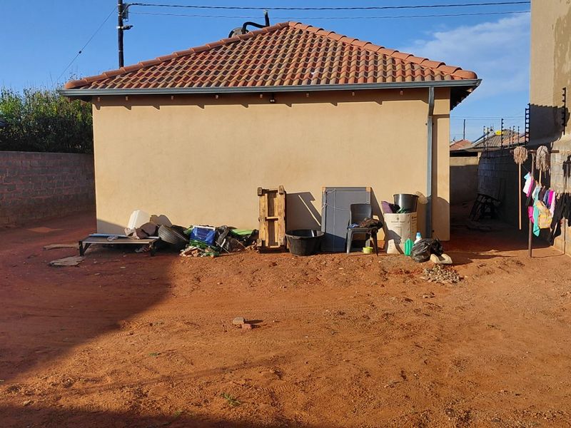 Rear exterior view of the property featuring a tiled roof, brick boundary walls with electric fencing, and an unlandscaped dirt yard area.