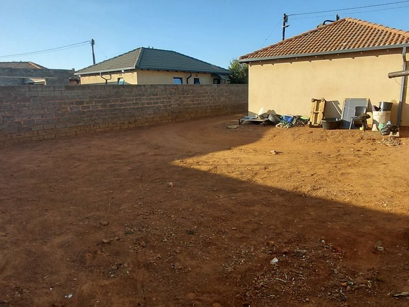 A spacious, unlandscaped rear yard featuring a perimeter brick wall and a detached structure with a tiled roof.