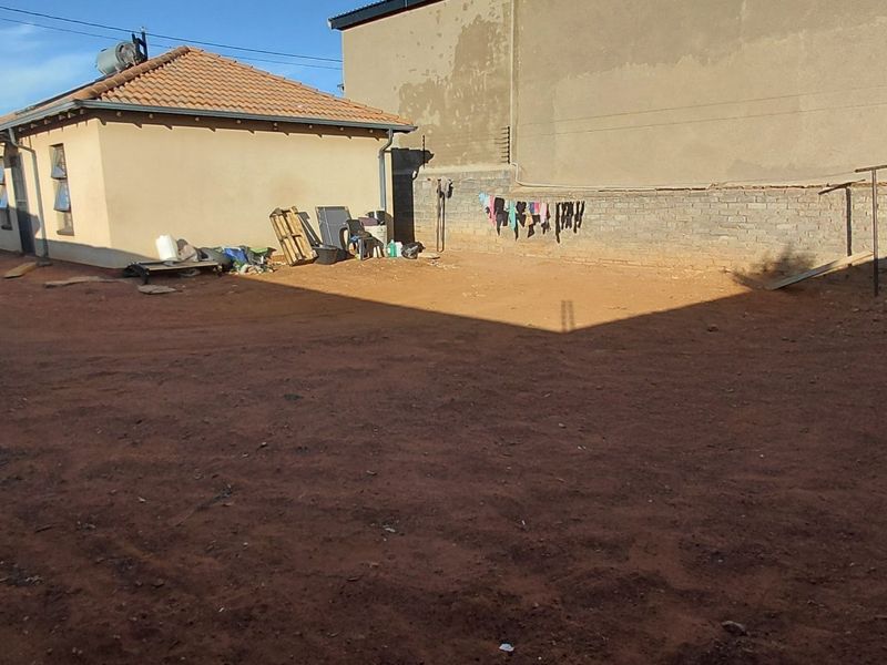 Spacious rear yard area featuring a brick boundary wall and access to the main dwelling with a tiled roof.