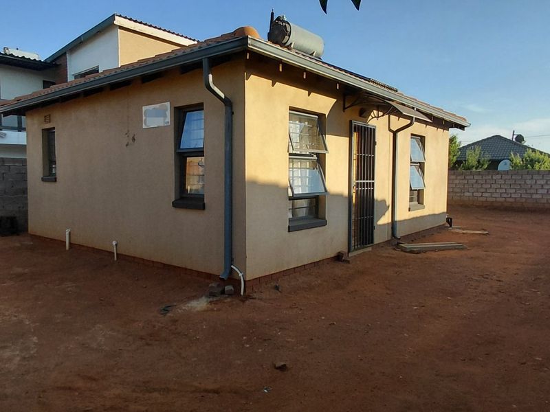 Rear view of a detached house featuring a solar water heater, security gate, and an expansive, unlandscaped yard enclosed by perimeter walls.