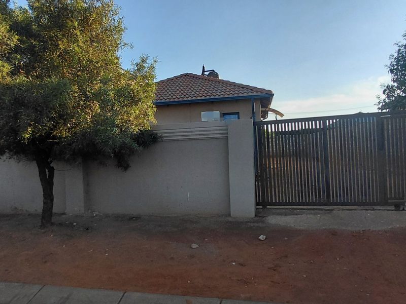 Front view of the property featuring a secure perimeter wall, slatted metal gate, and tiled roof structure.