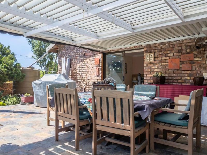 Covered outdoor patio area featuring a louvred roof, exposed brick wall, and slate tile flooring, providing a functional space for outdoor dining.