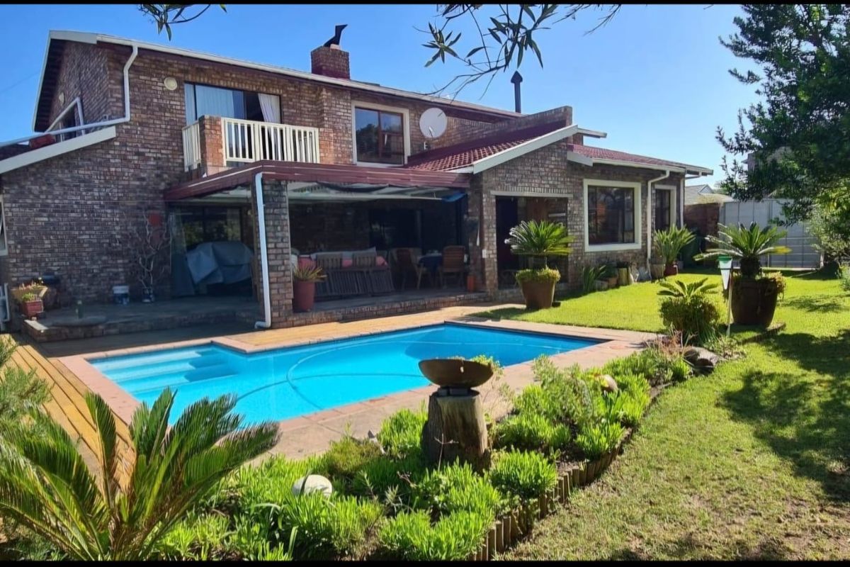 Rear view of a double-story brick house featuring a swimming pool, covered patio area, and a well-maintained garden.