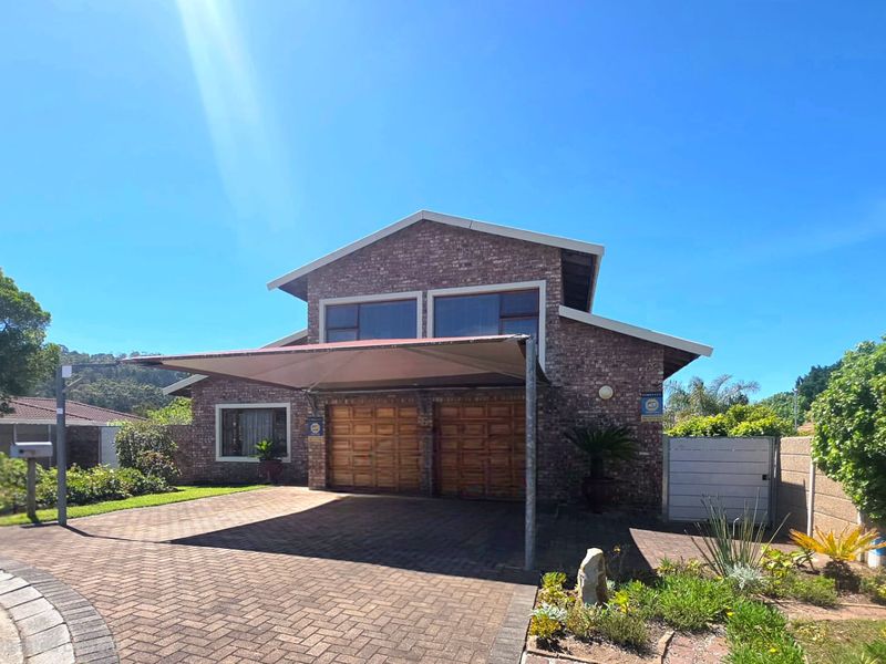Front elevation of a face brick house featuring a double garage with wooden doors, a paved driveway, and a shade sail carport.