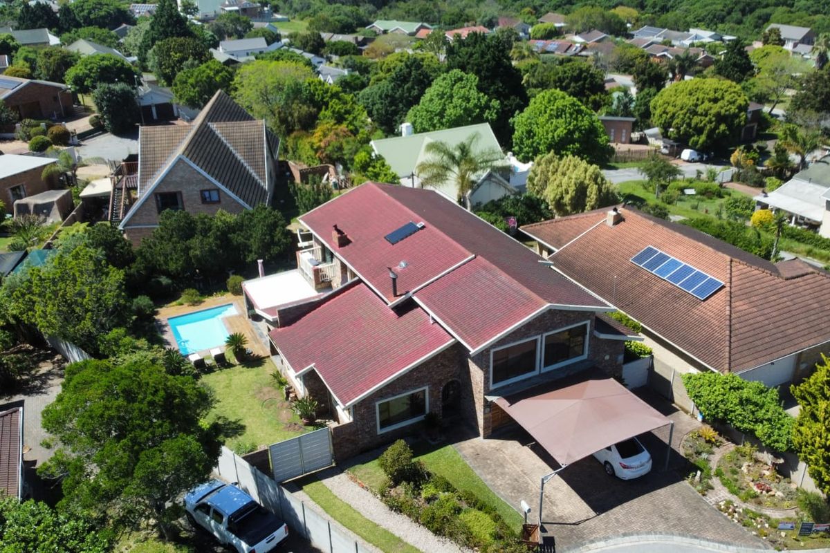 Aerial view of a residential property featuring a tiled roof, solar panels, a swimming pool, and a paved driveway with a carport.