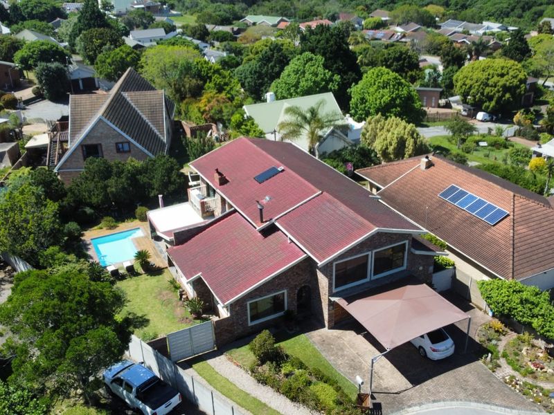 Aerial view of a residential property featuring a tiled roof, solar panels, a swimming pool, and a paved driveway with a carport.