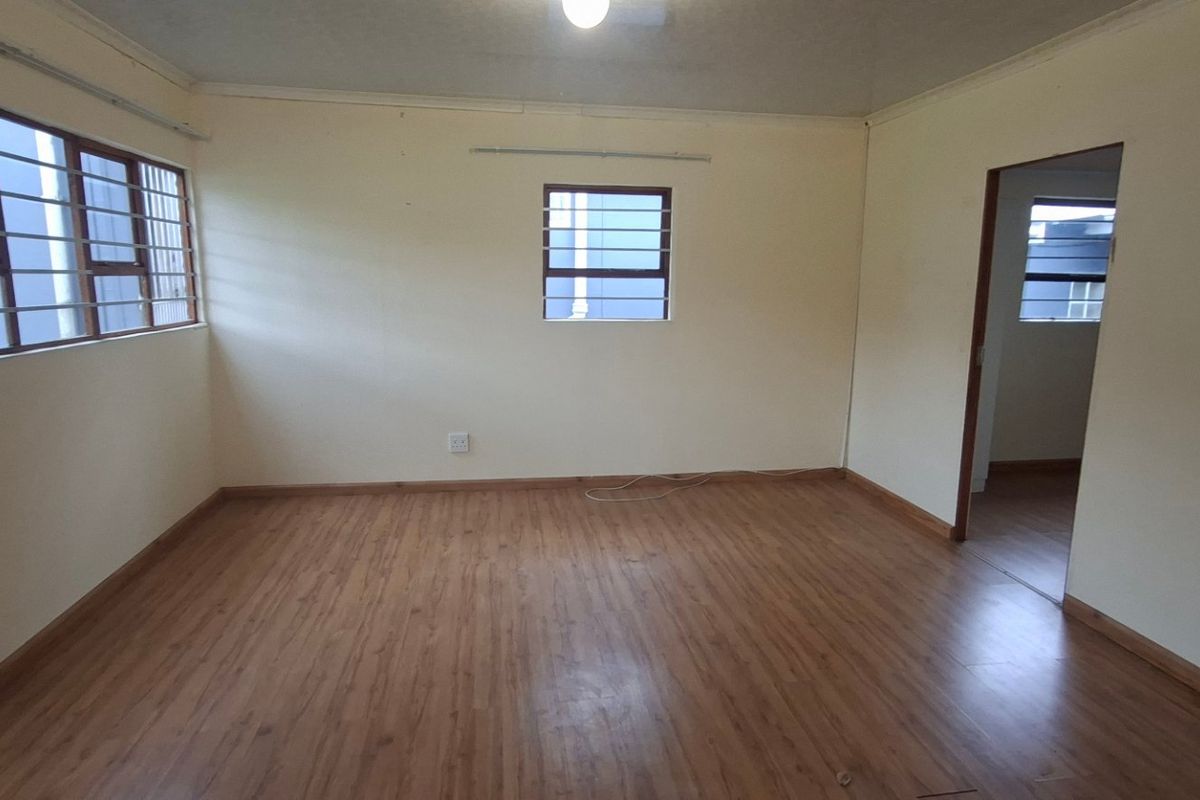A spacious, empty living area featuring laminate flooring, neutral walls, and windows fitted with security bars, offering a blank canvas for personalization.