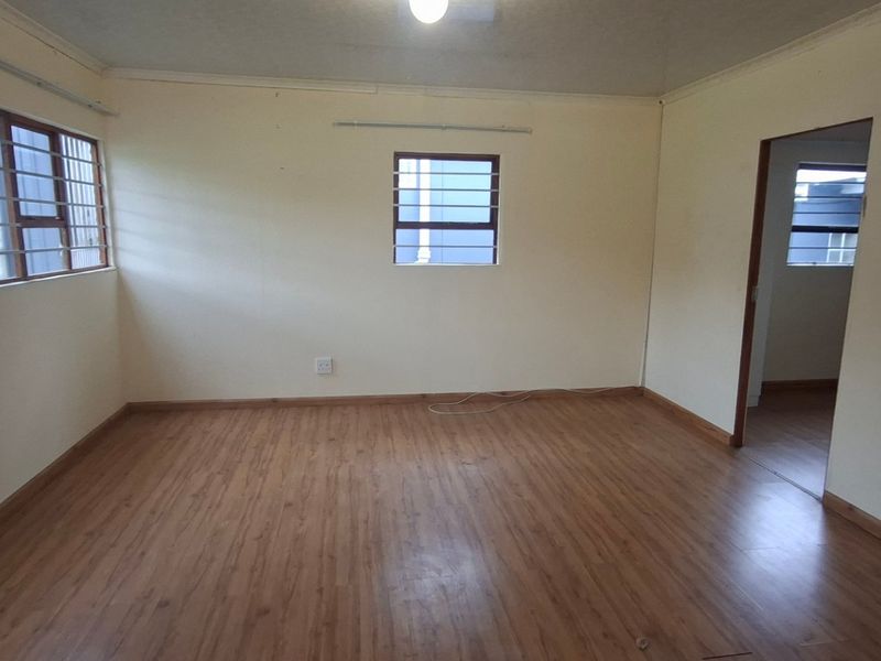A spacious, empty living area featuring laminate flooring, neutral walls, and windows fitted with security bars, offering a blank canvas for personalization.