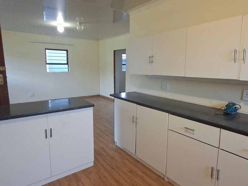A functional kitchen area featuring white cabinetry, dark countertops, and laminate flooring, offering a clean, blank canvas for potential updates or modern styling.