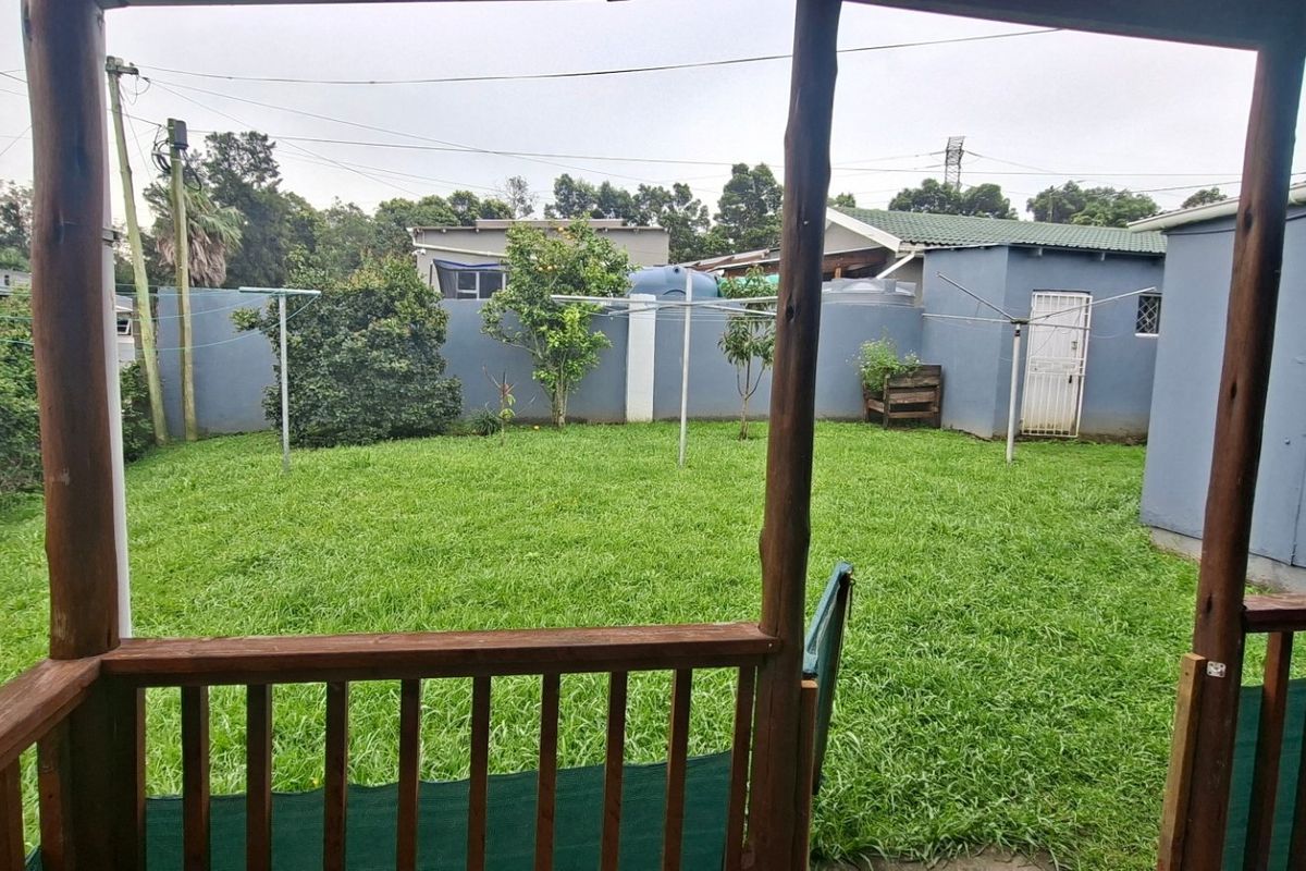 A view of the rear garden and lawn from a wooden deck, featuring a perimeter wall and clothesline.
