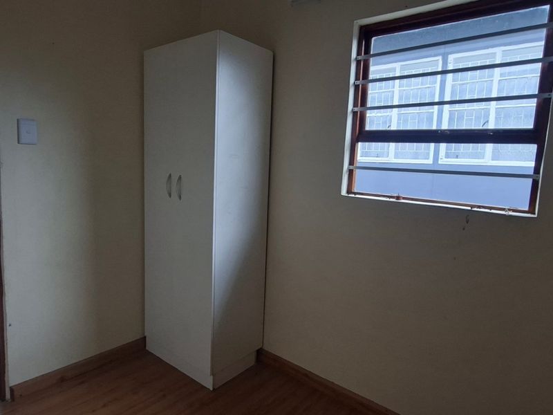 A simple bedroom featuring laminate flooring, a built-in cupboard, and a window fitted with security burglar bars.