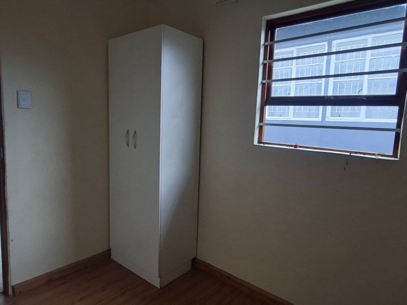 A simple bedroom featuring laminate flooring, a built-in cupboard, and a window fitted with security bars.