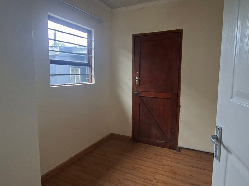 An empty bedroom featuring laminate flooring, a built-in wardrobe, and a timber door with security bars on the window.