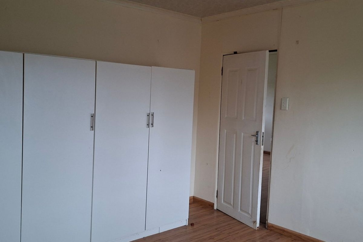 A bedroom featuring laminate flooring and built-in white cupboards, presenting a blank canvas ready for personalization.