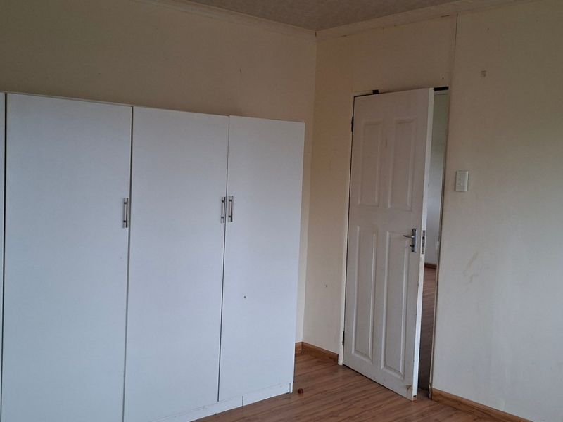 A bedroom featuring laminate flooring and built-in white cupboards, presenting a blank canvas ready for personalization.