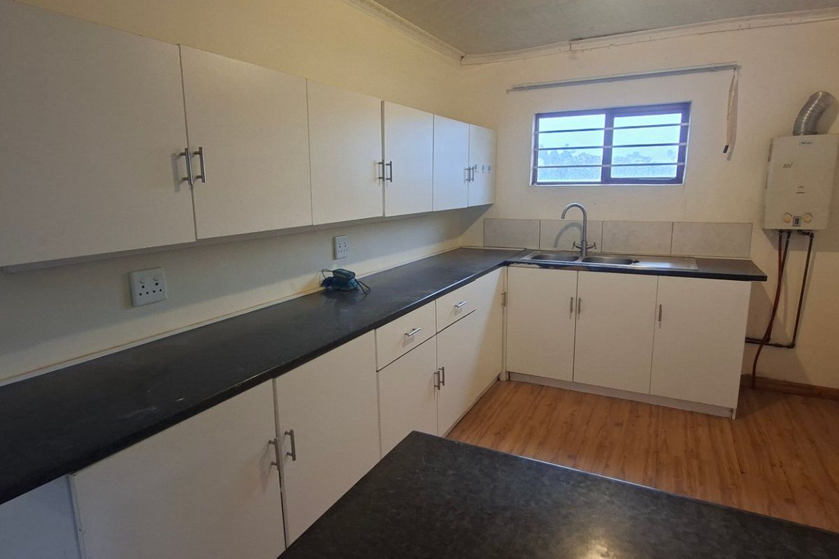A functional kitchen featuring ample white cabinetry, dark laminate countertops, a double sink, and wood-look flooring, offering a clean and practical workspace.