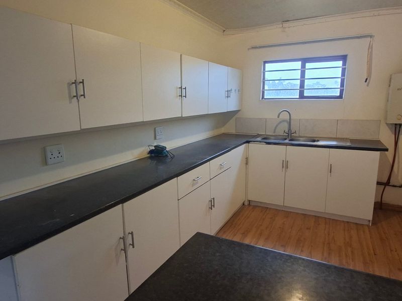 A functional kitchen featuring ample white cabinetry, dark laminate countertops, a double sink, and wood-look flooring, offering a clean and practical workspace.
