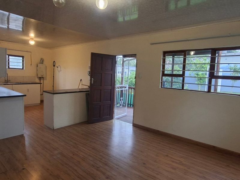 An open-plan living and kitchen area featuring laminate flooring, built-in cabinetry, and security bars on the windows.
