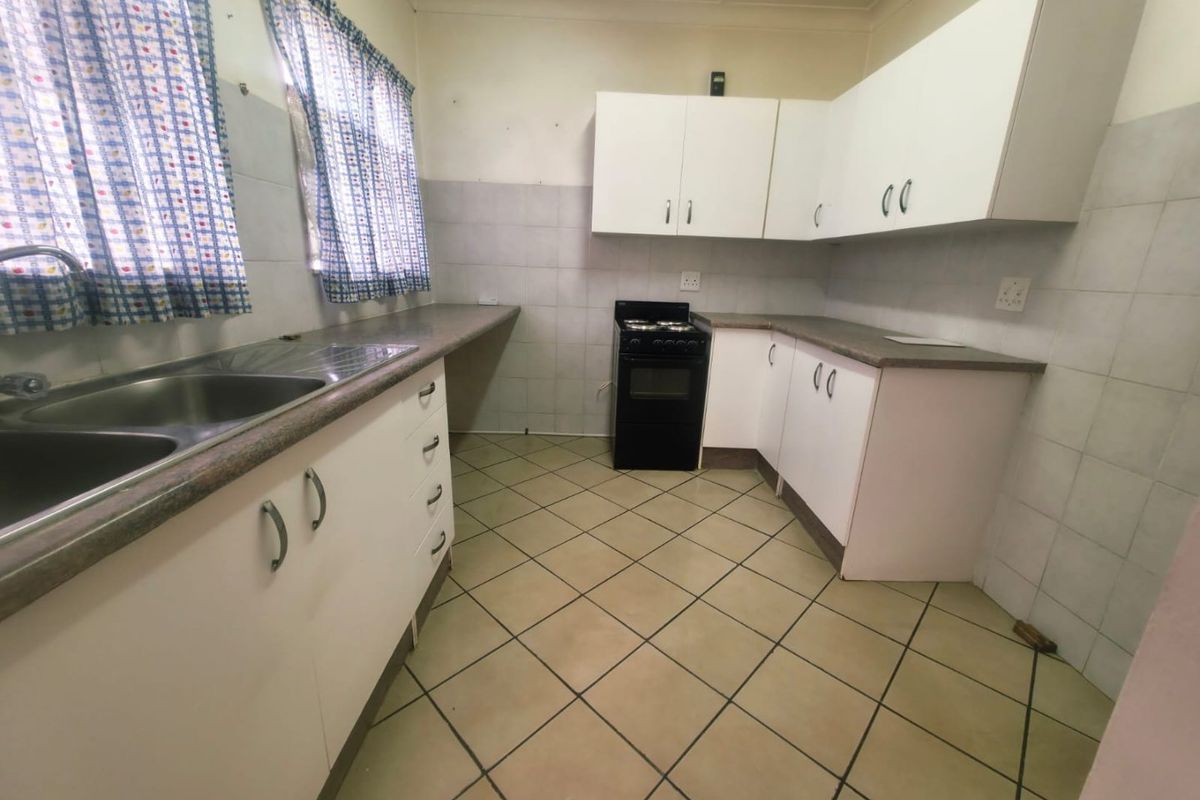A functional kitchen featuring white cabinetry, laminate countertops, a double bowl sink, and a freestanding stove with tiled flooring and splashbacks.