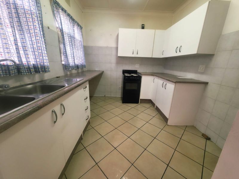 A functional kitchen featuring white cabinetry, laminate countertops, a double bowl sink, and a freestanding stove with tiled flooring and splashbacks.