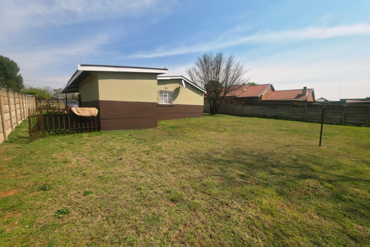 A spacious rear garden featuring a large lawn area, enclosed by precast concrete boundary walls and a metal gate.