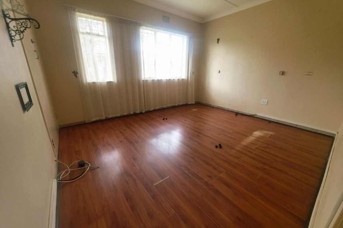An empty bedroom featuring laminate flooring, large windows with security bars, and neutral wall finishes, ready for new occupants or renovation.