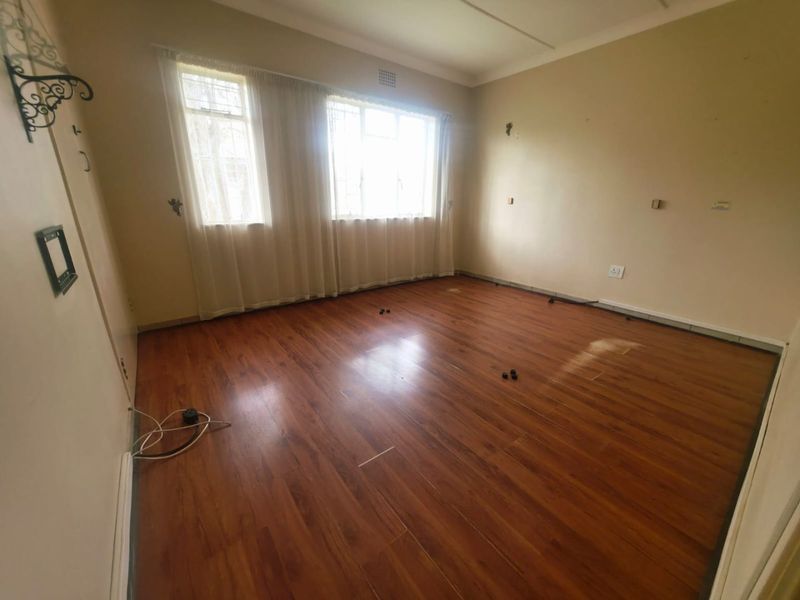 An empty bedroom featuring laminate flooring, large windows with security bars, and neutral wall finishes, ready for new occupants or renovation.