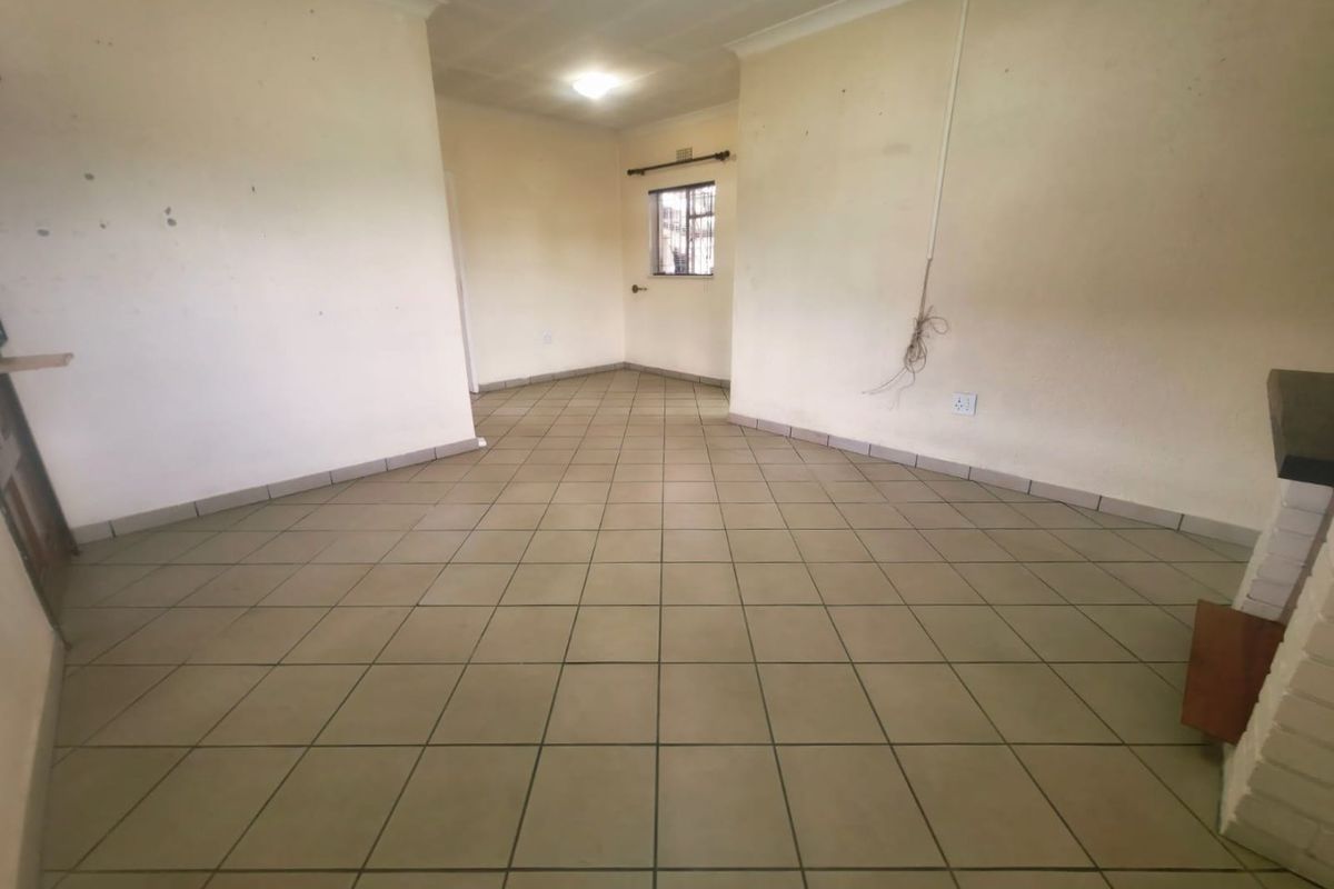 An empty living room featuring tiled flooring, a brick fireplace, and a window with security bars, requiring cosmetic updates to the walls.