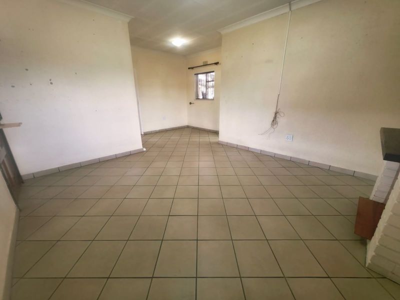 An empty living room featuring tiled flooring, a brick fireplace, and a window with security bars, requiring cosmetic updates to the walls.