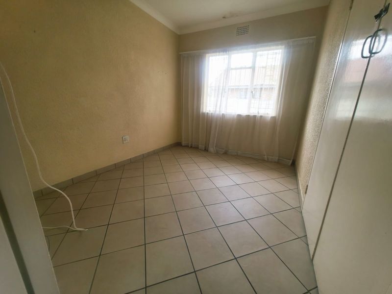 An empty bedroom featuring tiled flooring, a built-in cupboard, and security bars on the window, ready for a fresh coat of paint.