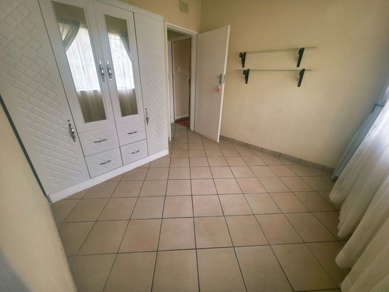 A clean, empty bedroom featuring tiled flooring and a large built-in wardrobe with mirrored panels.