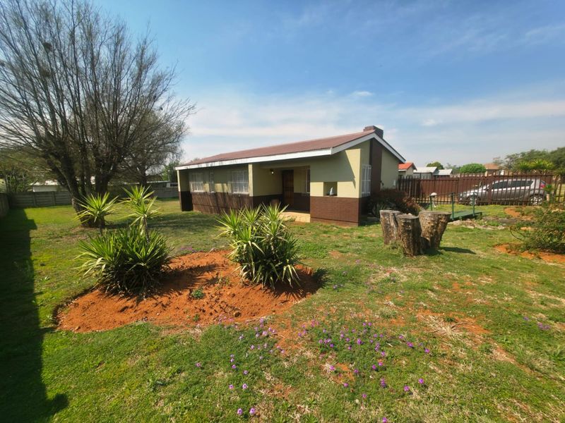 A detached single-story house featuring a metal roof and security bars, set within a spacious garden with a lawn and perimeter walling.