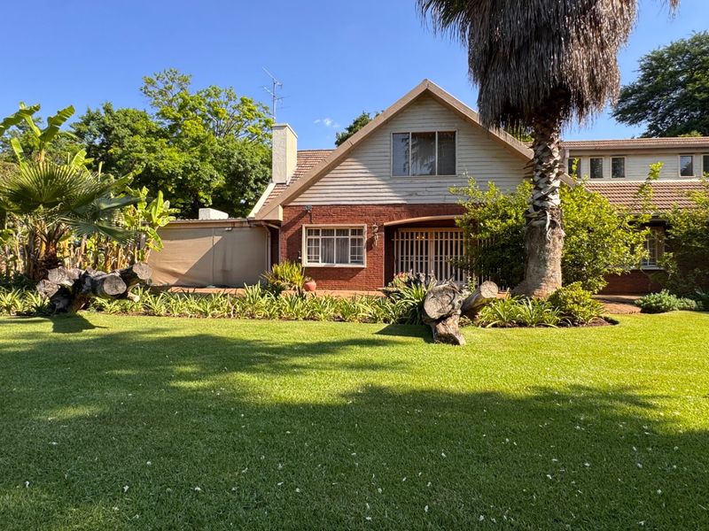 A view of the rear elevation featuring a brick and timber facade, tiled roof, and a well-maintained garden with mature trees.