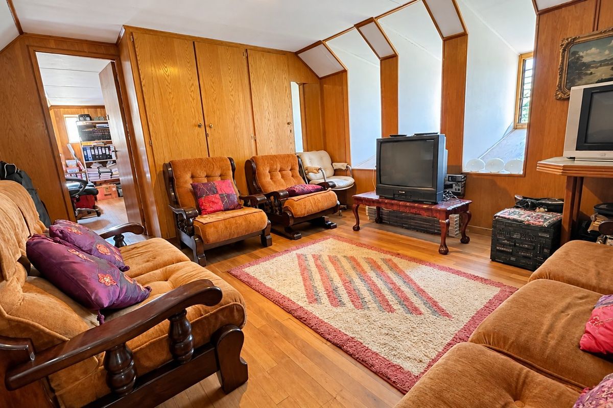 A living room featuring warm wood paneling, built-in cabinetry, and hardwood flooring, with a unique sloped ceiling design.