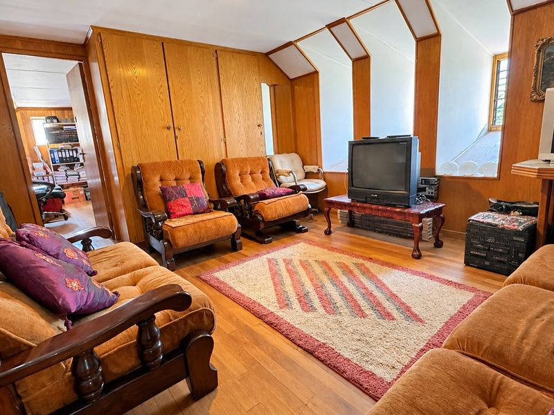 A living room featuring warm wood paneling, built-in cabinetry, and hardwood flooring, with a unique sloped ceiling design.